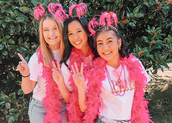 Three women with pink feather boas, holding up one,two and three fingers.
