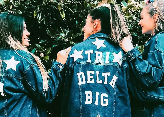 Women with denim jackets that read 'Tri Delta Big' on the back.
