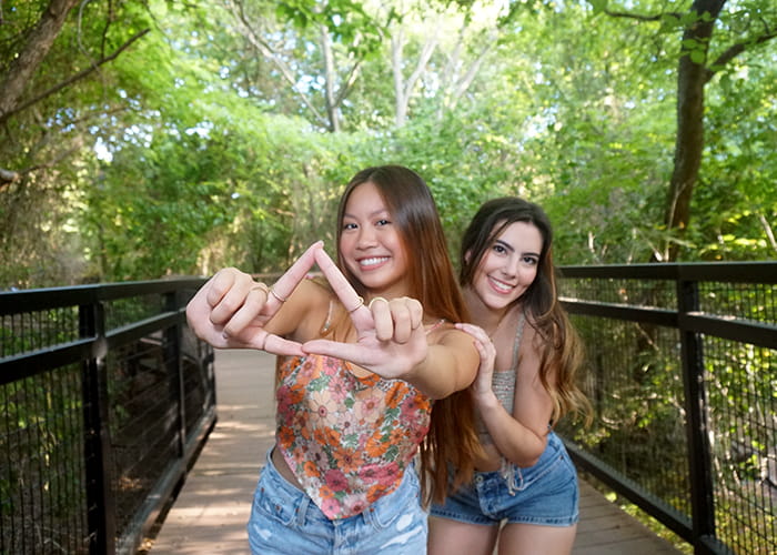 Two women on a bridge, one making a tri delta hand symbol.